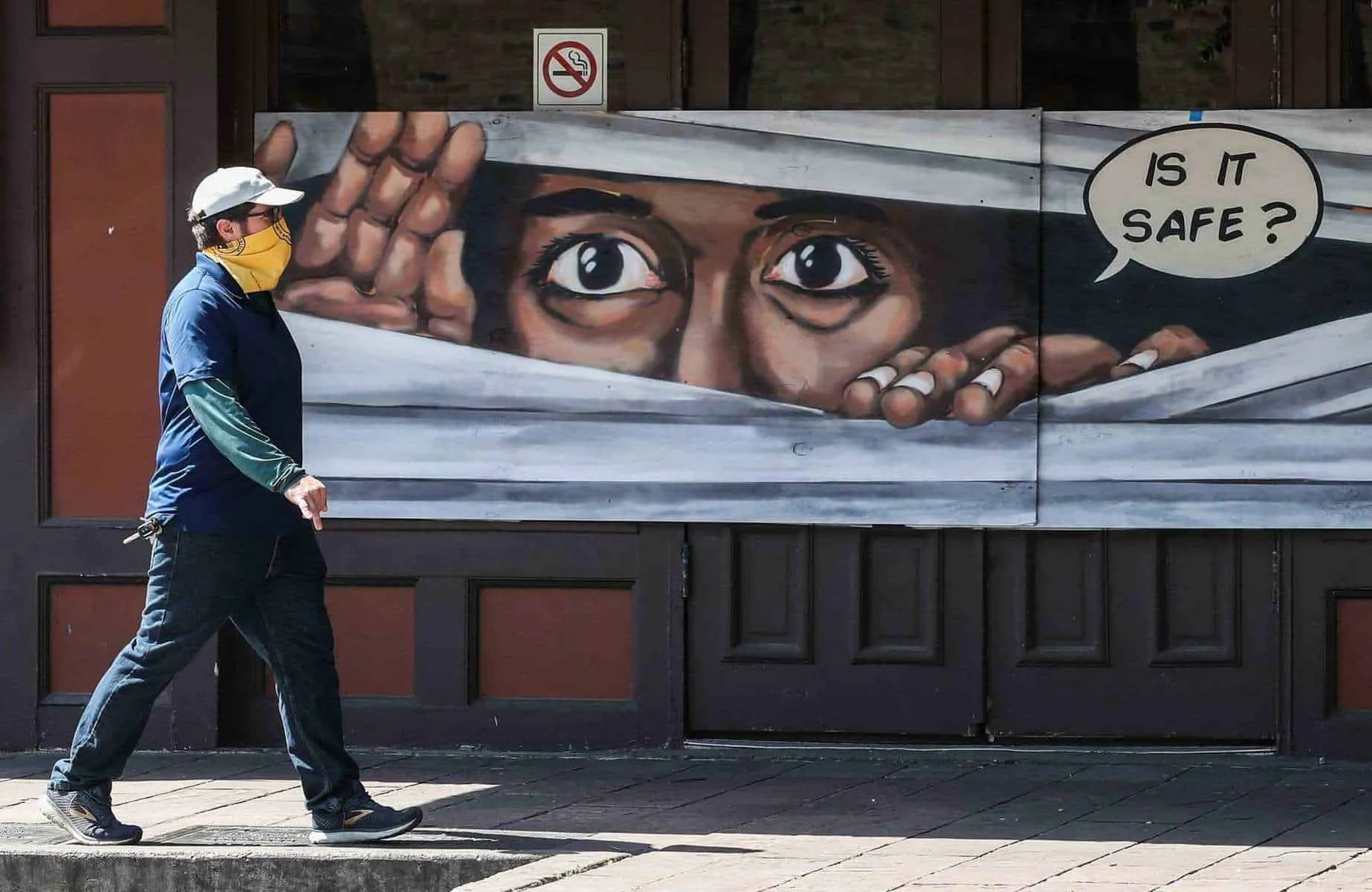 A man walks in front of a mural on 6th Street wearing a mask. [LOLA GOMEZ / AMERICAN-STATESMAN]